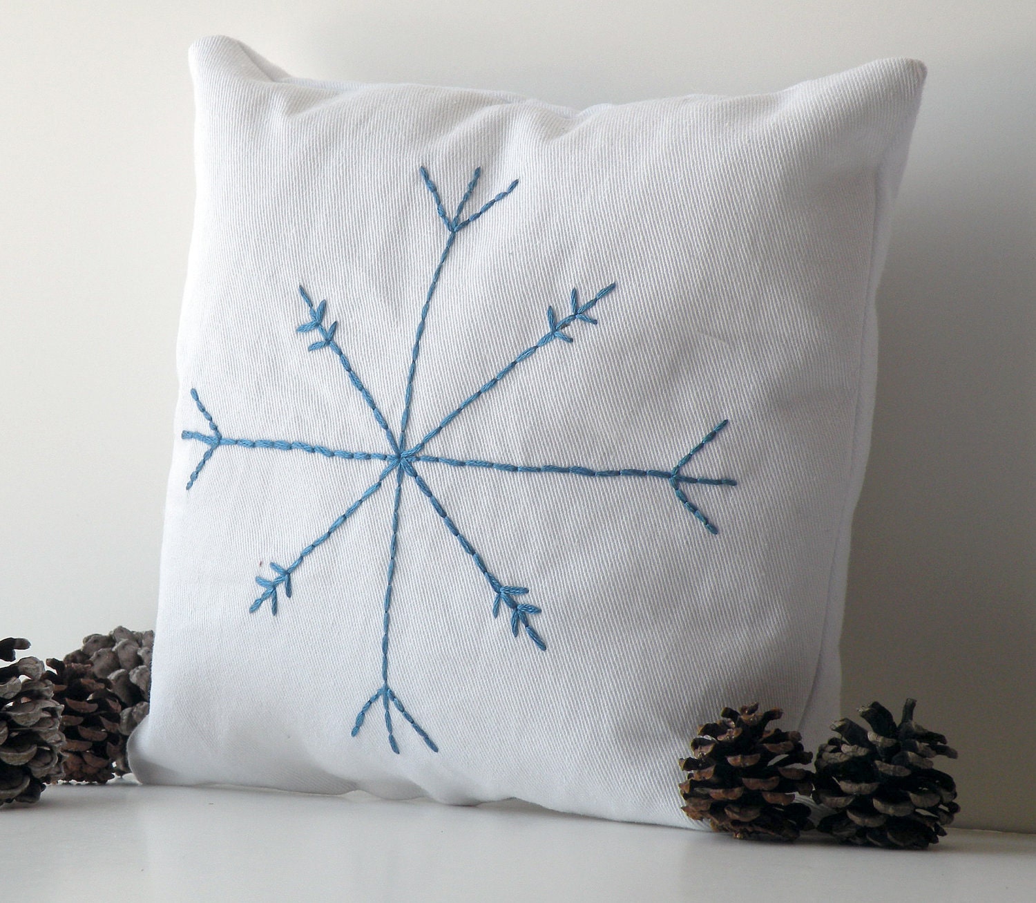 Small white cotton decorative pillow with blue embroidered snowflake