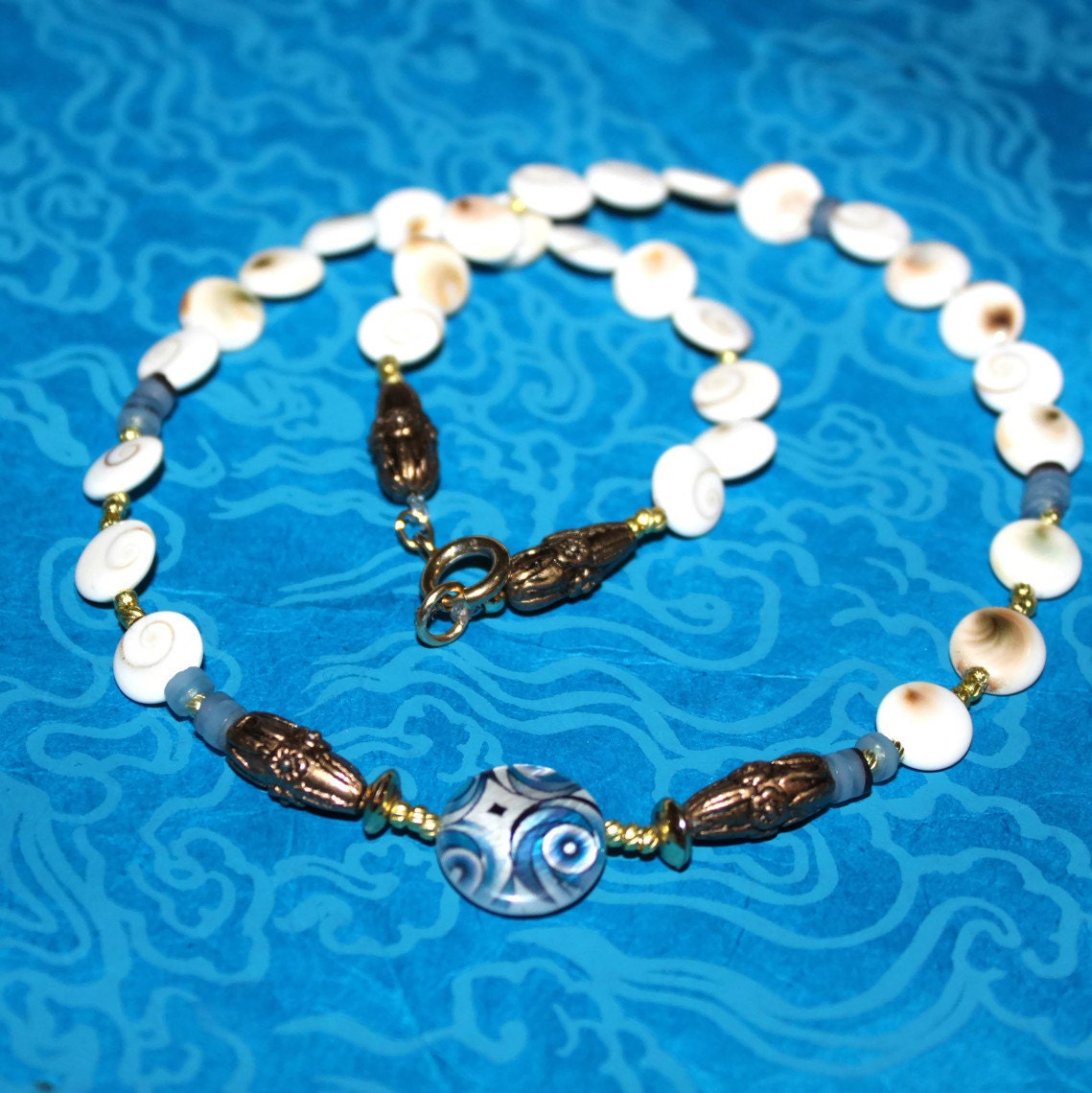 HOLDING for L's hubby - beaded necklace-decorative blue flat round shell- white brown Shiva eye disc- dark blue hammer shell Heische