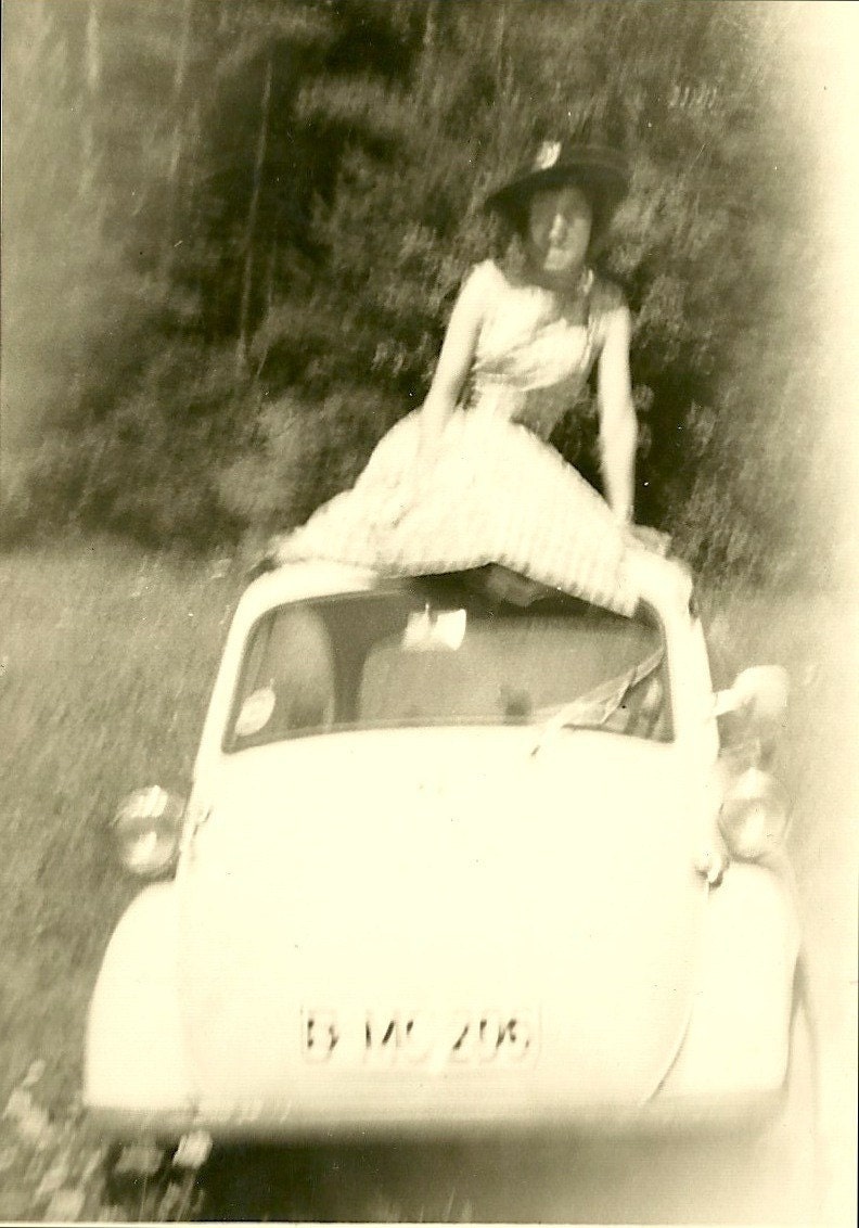 Vintage black and white 1950s photo of some blurry people and a car