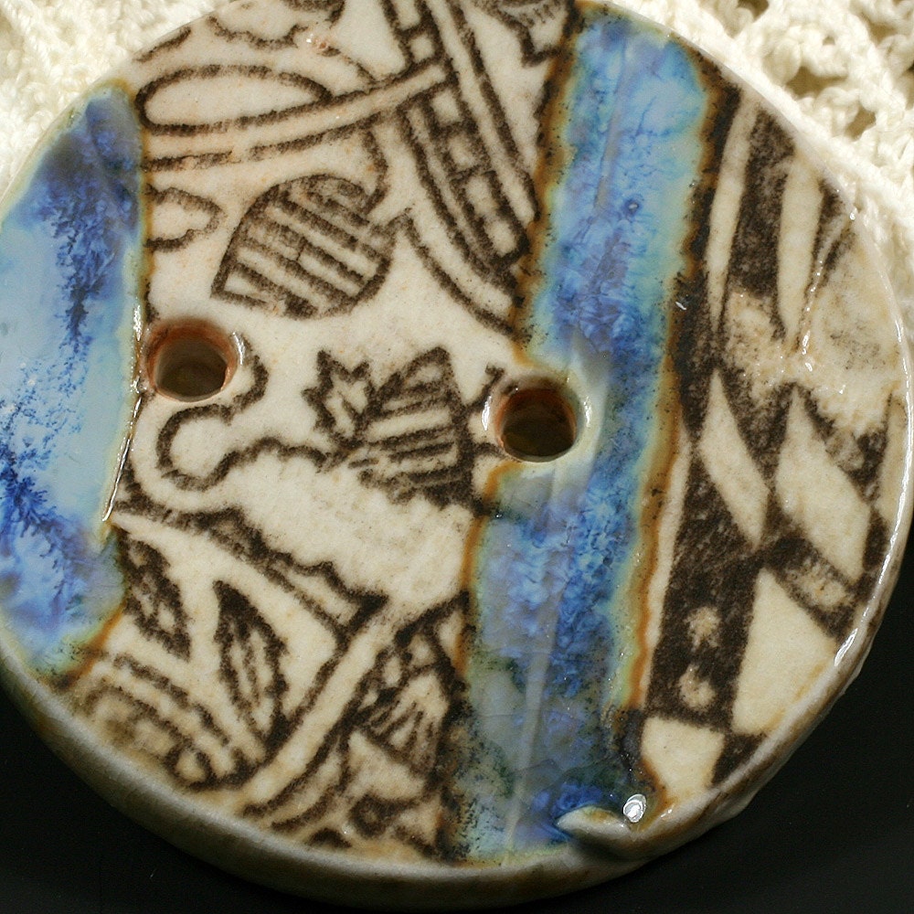 Handmade porcelain button, black graphic, white background with tinges of orange, two blue glaze accents. EB153