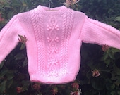 Girl's handknit pink aran sweater with back opening.