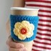 Blue coffee cozy with yellow flower and red button by The Cozy Project