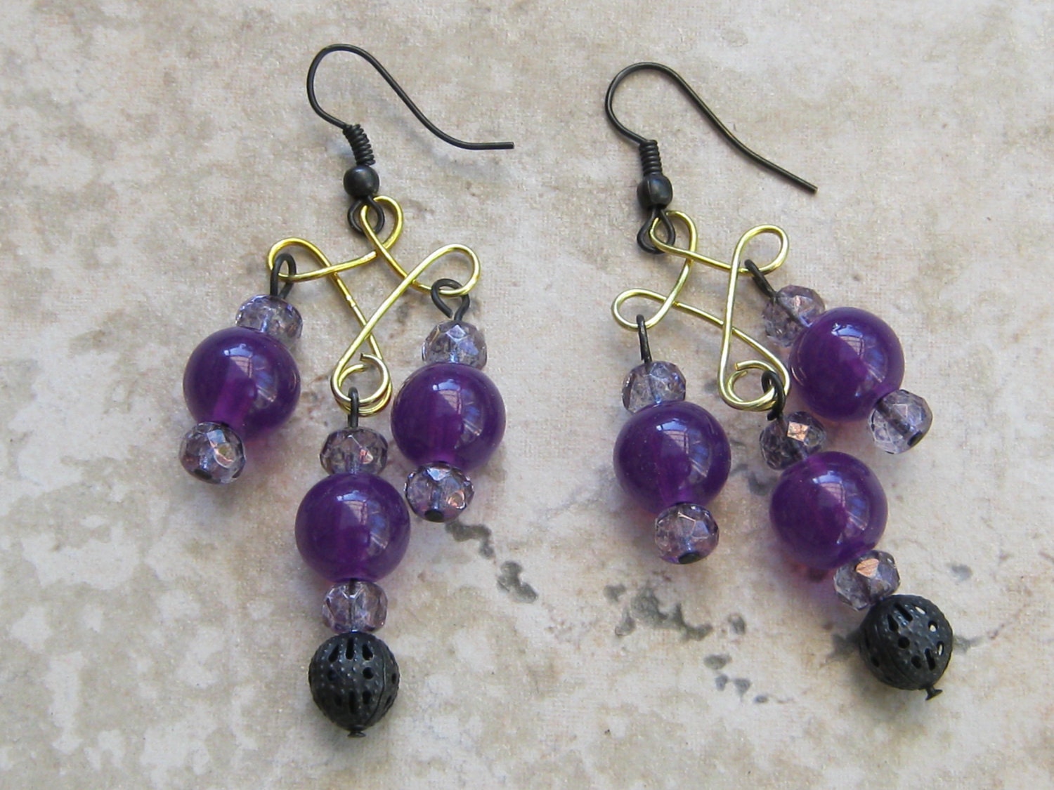 Chandelier earrings of grape purple jade beads, rondel cut crystal beads, black ear wires, brass bead holders and a hollow black lacy bead.
