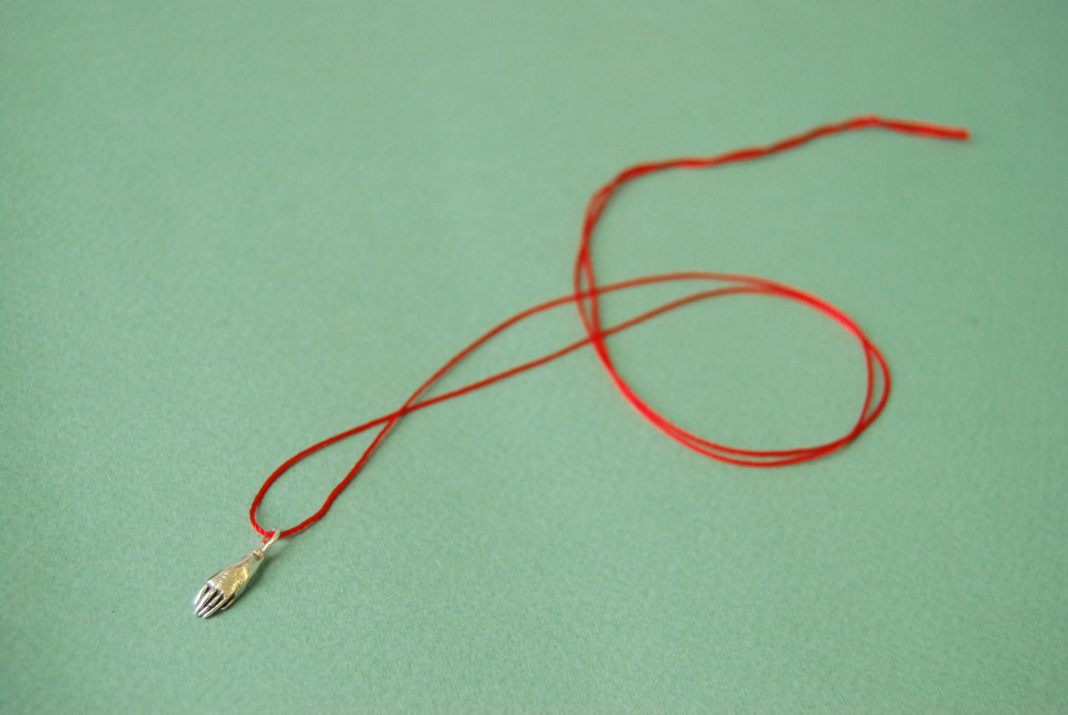 Silver hand on red silk cord