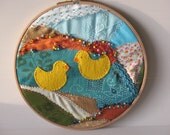 embroidery hoop, fibre art, fabric collage,  two yellow ducks swimming in a pond on a crazy quilt background -