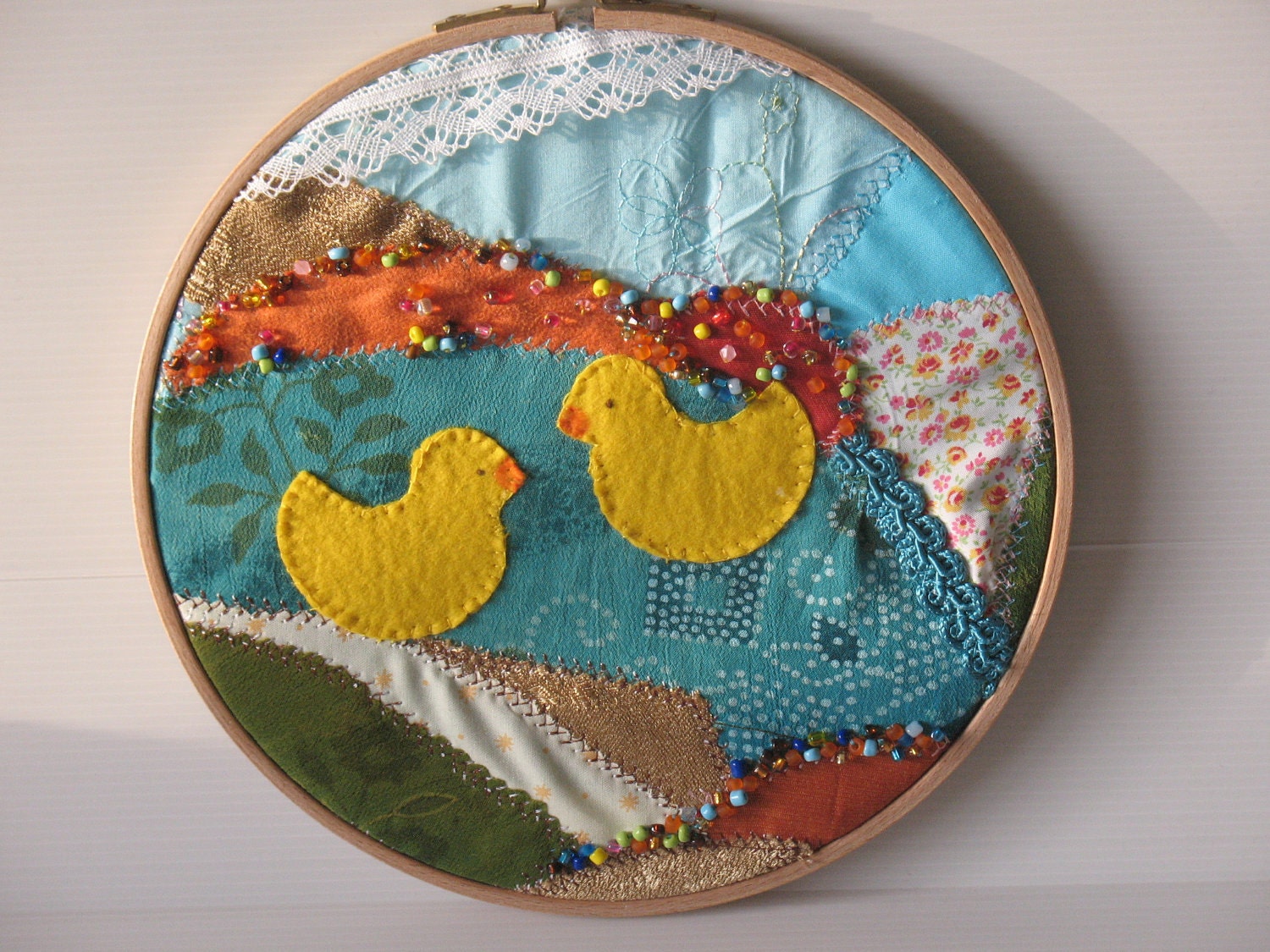 embroidery hoop, fibre art, fabric collage, two yellow ducks swimming in a pond on a crazy quilt background -