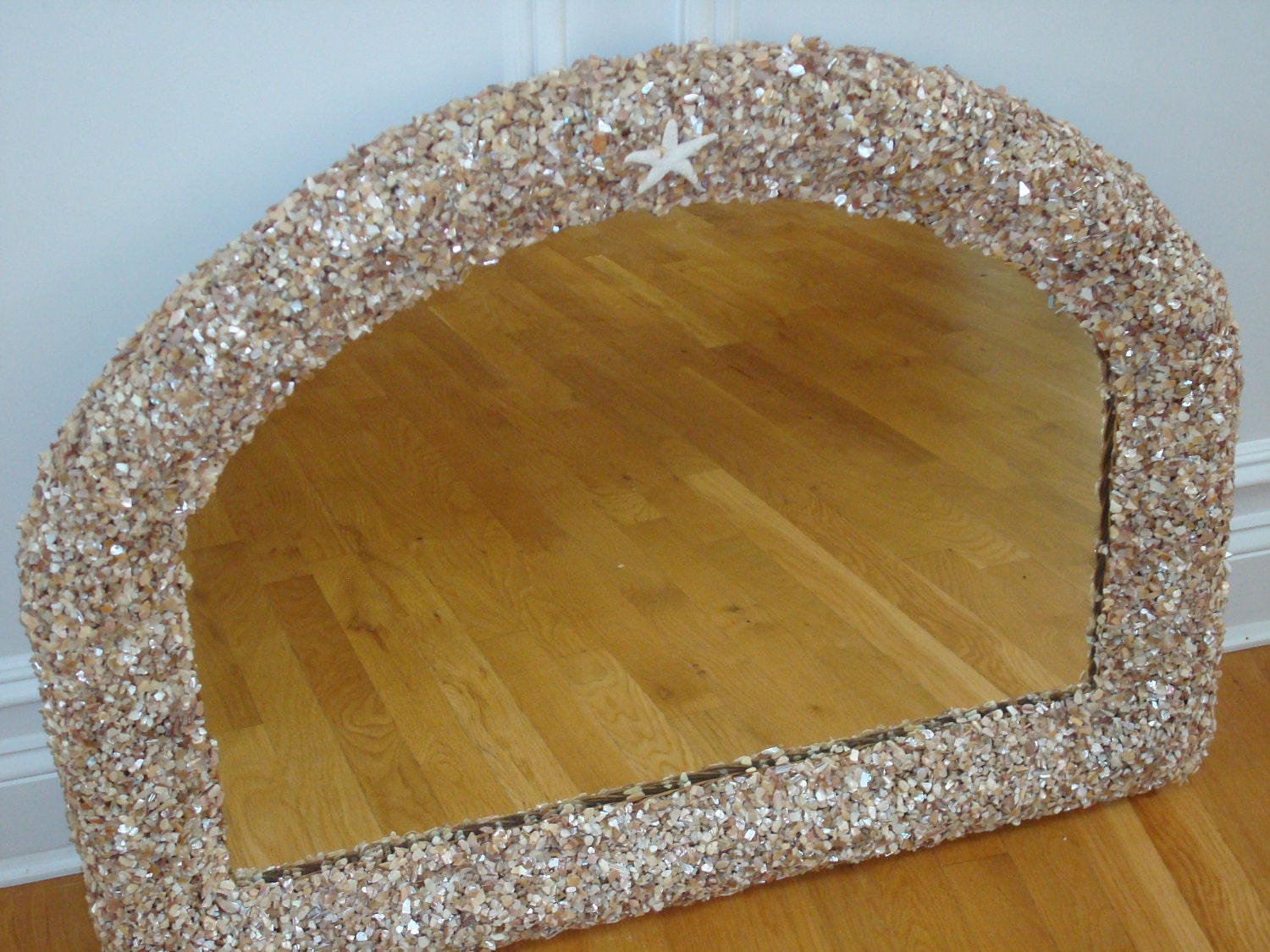 Large arched mirror updated with sea shell fragments.  At the top center of the mirror is a small bleached star fish.
