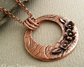 Antiqued copper necklace featuring a circular pendant with hand sculpted flowers and leaves