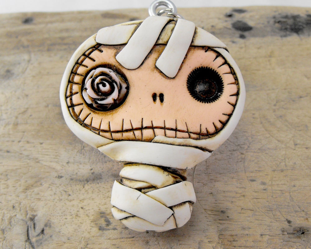 Adorable baby mummy keychain in dirty white. Creepy and cute baby skull with a pink rose inside his eye.