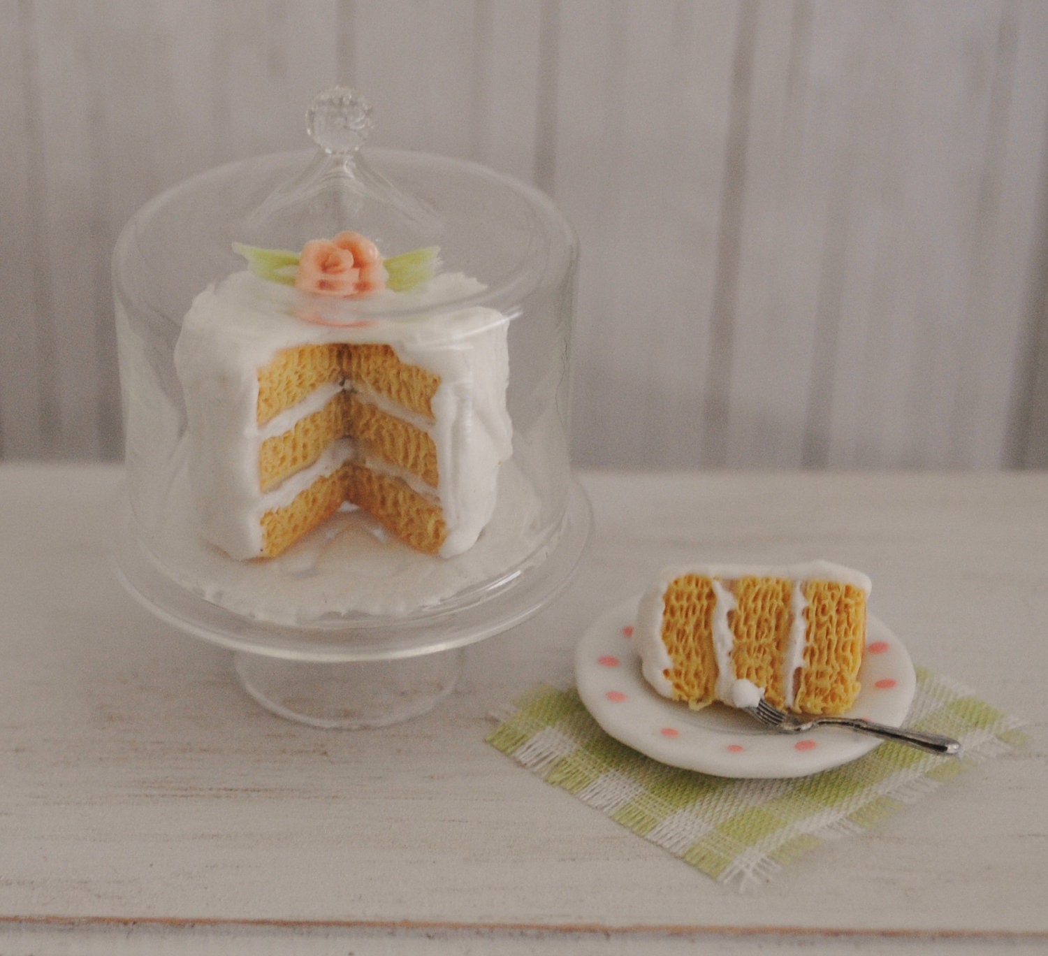 Miniature Layer Cake With Creamy Icing And A Pink Rose On A Covered Glass Cake Stand And A Slice Of Cake