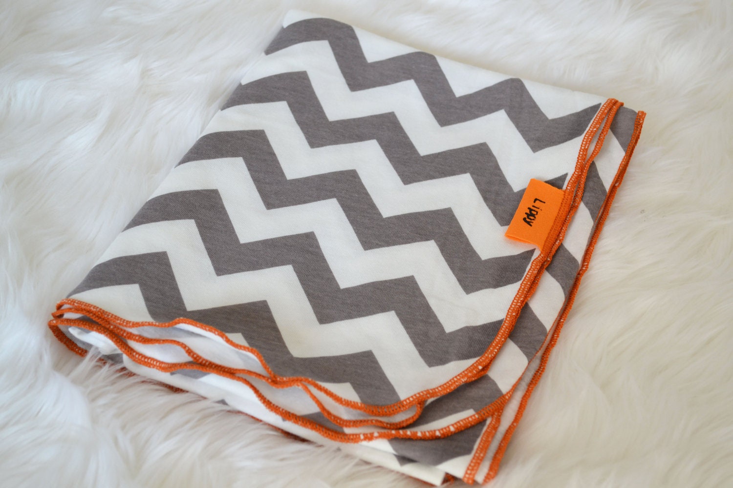 Chevron baby swaddler. Blanket size: Size 31 by 40 inches. Colors- gray and white with orange edging.