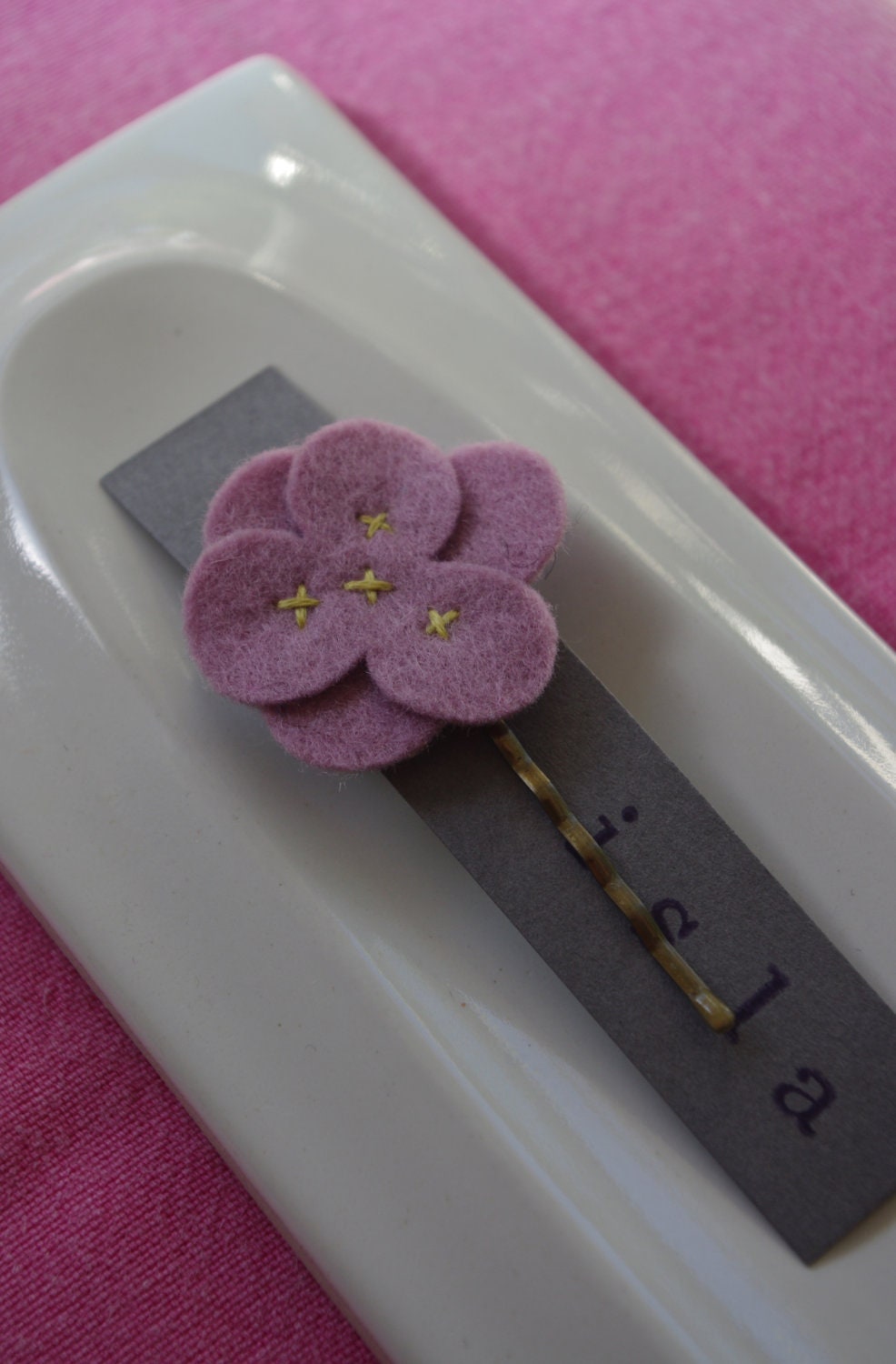 Rose wool felt flower hair clip with yellow stitching.