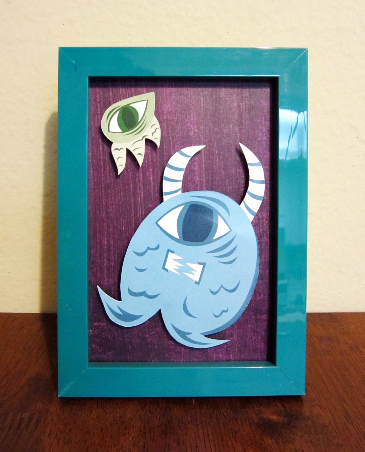 Cyclops Monster Duo 2 - Colorful Cut Paper Framed Wall Art - Purple, Blue, Green with Teal Frame