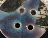 Handmade porcelain button, black graphic against buff background, teal and lilac accent glaze. (EB194)