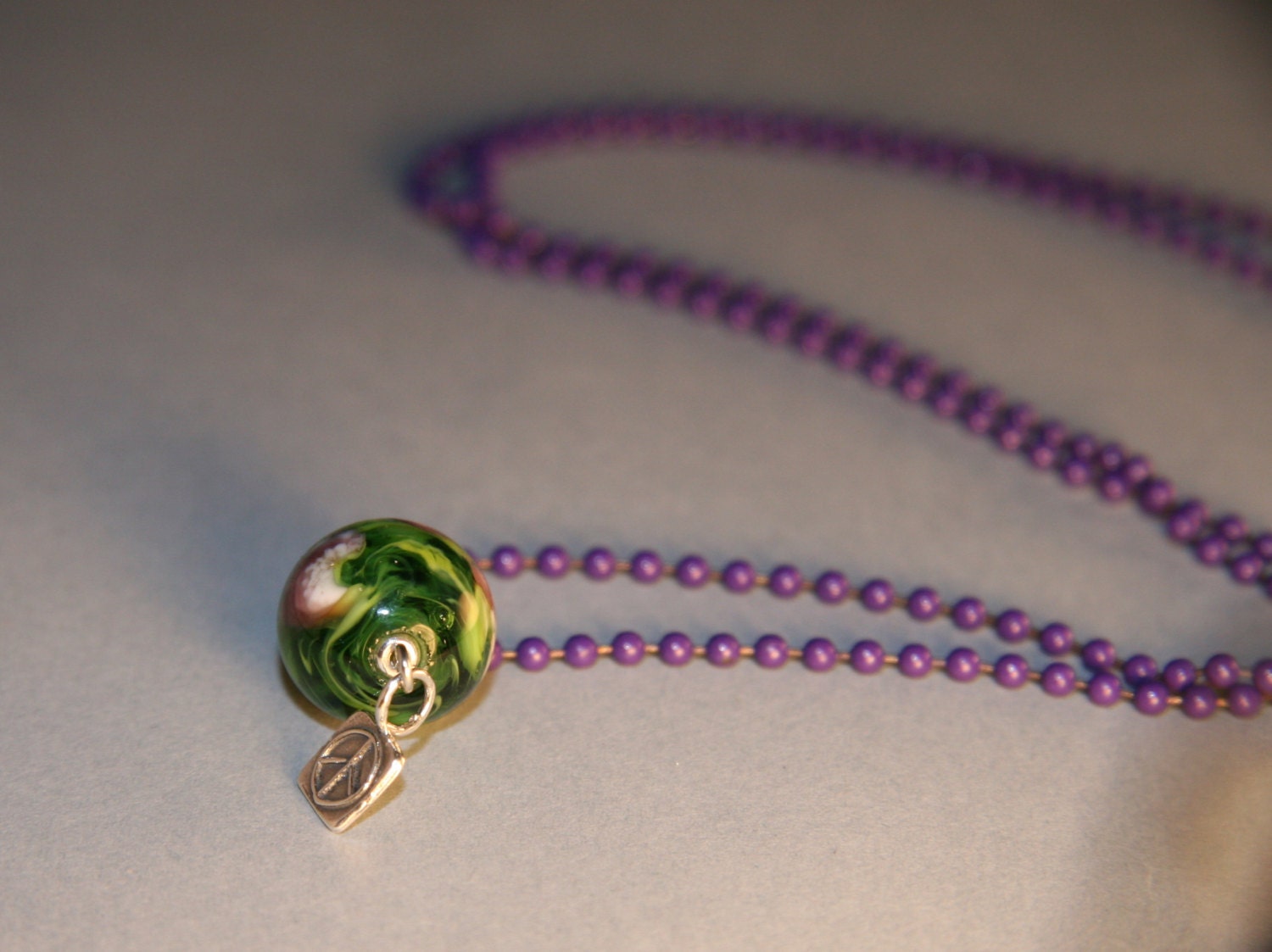 A necklace, green and purple handmade glass bead, purple bead chain, sterling silver peace sign