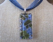 Pressed  Kelly  Green Four Leaf Clover with the lovely Periwinkle Forget- Me- Nots .  Handcut Rectangle Glass. 1x2 inches.