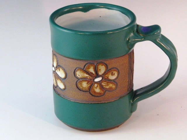 Green mug with flowers carved around center of pot.