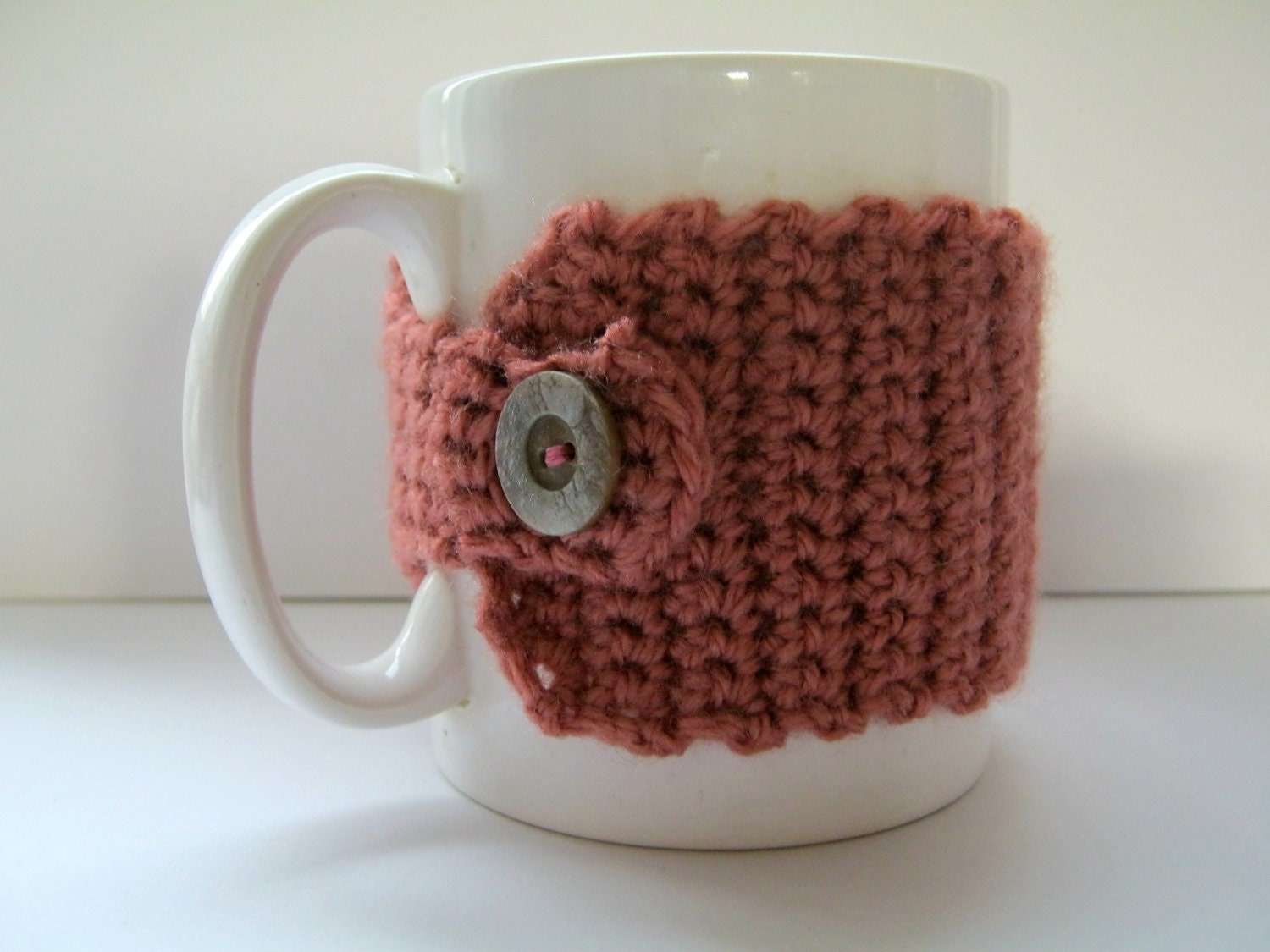 Crocheted mug cosy in salmon pink with silvered wood-effect button