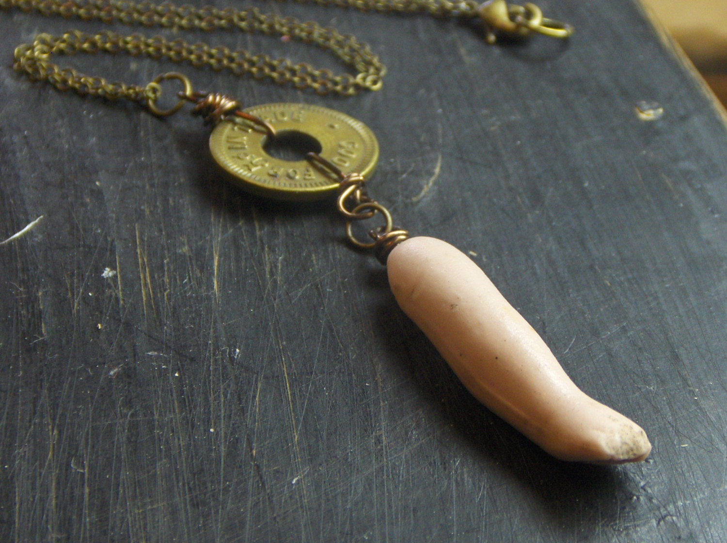 PENNY ARCADE. Vintage ceramic bisque doll arm and game token curiosities necklace.