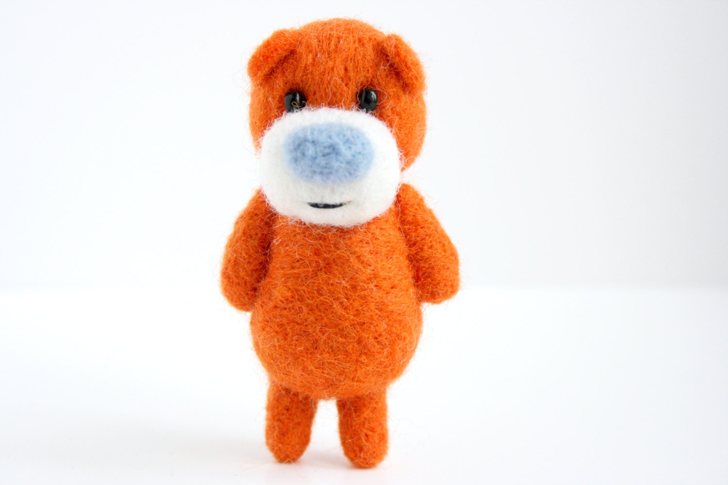 Needle felted orange pocket bear with a light blue nose
