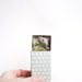 Tiny gray mouse in a matchbox. Scale dollhouse miniature, sleeping mice in bed. Pastel gray, green leaf.