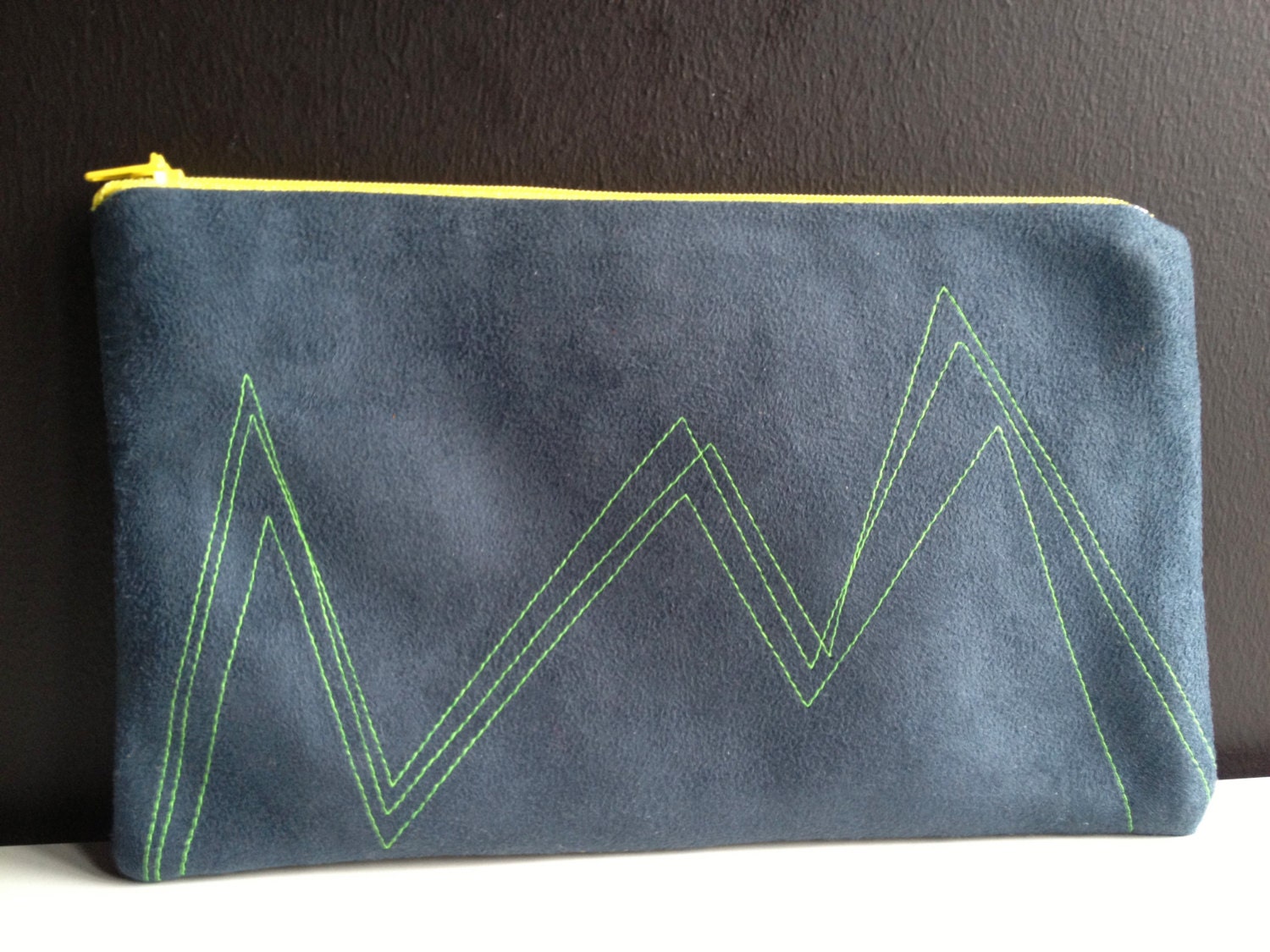 dark blue pouch made of faux leather with stitched geometric lines in neon green