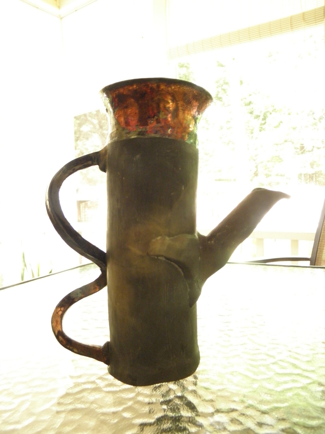 Dull gray and black body with a raku handle and top in copper and green glaze
