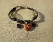 Gypsy Charm Bracelet. Funky Clay Face and Bronze Spiral Charms. On Denim Blue Twine & Forest Green Organza Ribbon.