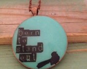 Aqua blue resin pendant necklace with a black bird and quote 'born to stand out'. Large round 38mm
