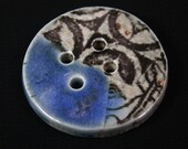 Handmade porcelain button, black graphic against smokey background, blue accent glaze. (EB232)