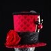 Red and Black Scaled Fabric Mini Top Hat Fascinator with Red Flower, Elegant Hat Pins, and Black and White Feather Accents.