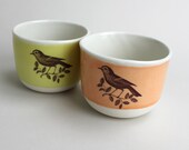 two wee tea cups one in pale orange, one in mustard, with early birds