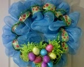 Poly Deco Mesh Easter Wreath blue with yellow polka dotted ribbon surrounding easter eggs that are nestled in the vibrant green flowers.