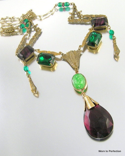 Vintage Egyptian Revival Art Deco festooned necklace with green and purple glass. Incredible necklace! Measures 25-1/2 inches in length. Dramatic purple glass and green scarab add another 4 inches. Festooned necklace has winged findings and lotus centerpiece. All brass and glass appear to be in very good condition. Decorative push in clasp is working perfectly.