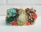 Vintage brass cuff bracelet embellished with a beautiful green cameo in a bezel with glass leaves, enamel flowers, crystals, leaves,and a b