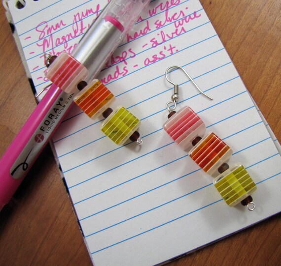 three acrylic cubes of alternating white and colored stripes, separated by matte purple glass beads; from top to bottom the color stripes are pink, orange, yellow