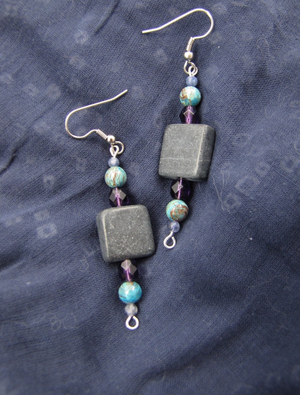 central square of blackstone, with symmetrical beads on either side: faceted purple glass dodecahedron, swirly blue-and-brown 6mm jasper bead, tiny iolite bead