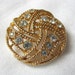Gold tone brooch pin with intertwined circles and clear rhinestones.