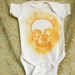 Glittery orange skull hand painted on a white Rabbit Skins cotton newborn onesie