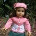 Handknitted, peachcolored sweater with flower design and matching hat and a green A-line skirt for American Girl doll and other similar 18"