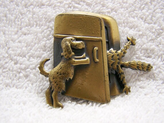 Dog is slamming the refrigerator door closed leaving half a cat sticking out.  Vintage JJ cat brooch.