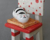 Black and White Ceramic Cat in Sleeping on a Red and White Chair - Ceramic Sculpture