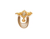 Gold tone brooch features a rhinestone studded pin and ornate dangling pendant with a large centeral cabochon