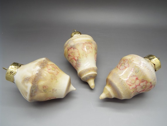 Three ceramic Christmas ornaments in a yellow and purple glaze, with a delicate pink floral design.