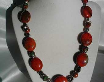 Statement necklace containing red beads with green accents along with metal beads.