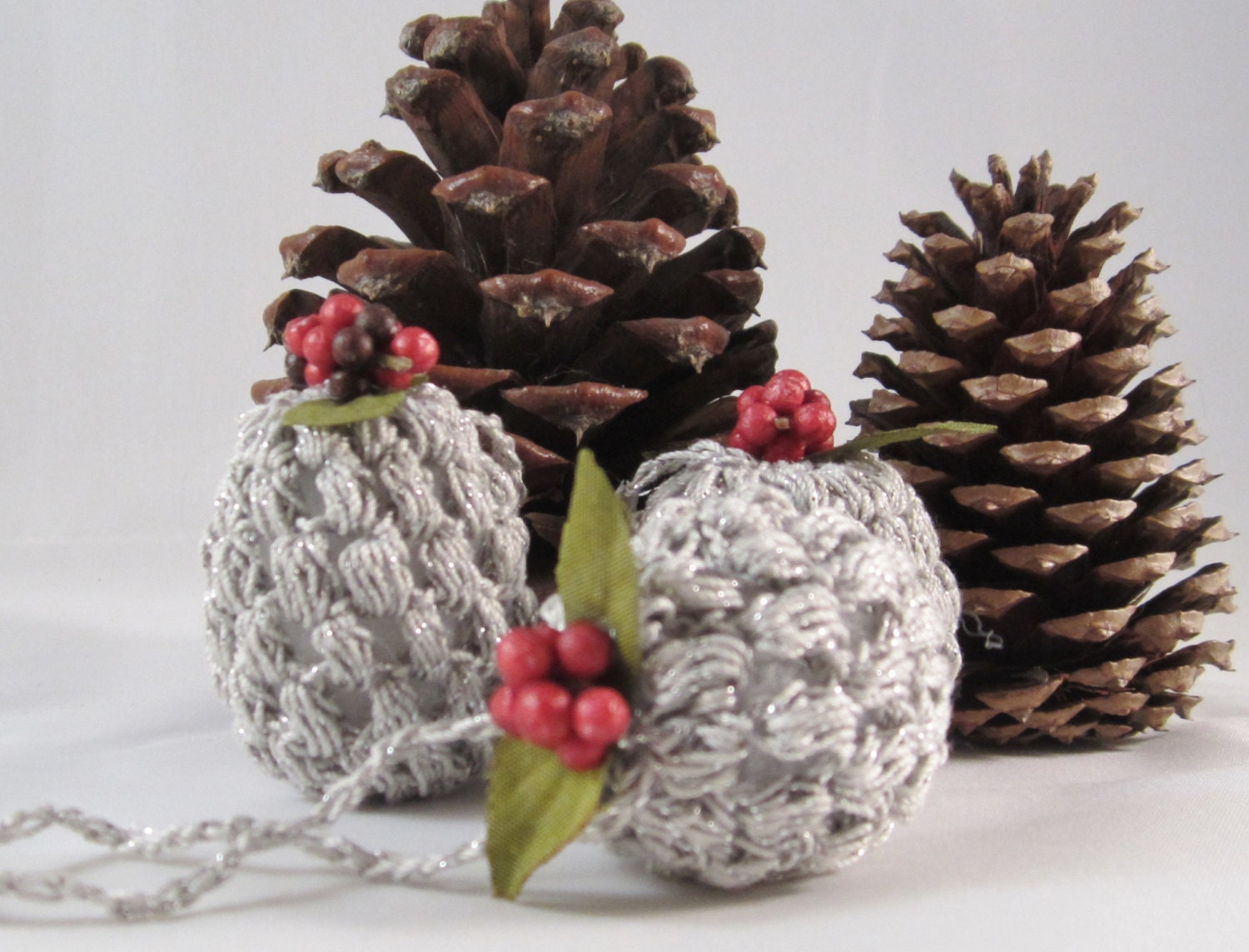 Christmas Ornaments-these petite pinecones are handcrochet with a silver glitter yarn & are embellished with green leaves and red berries.