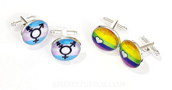 Photo of two pair of cufflinks, one with a rainbow design, and one with the trans flag and trans symbol.