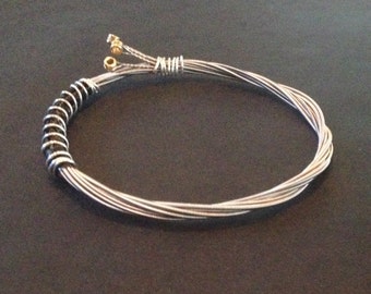 A handmade recycled guitar string bracelet/bangle bound with silver coloured wire.