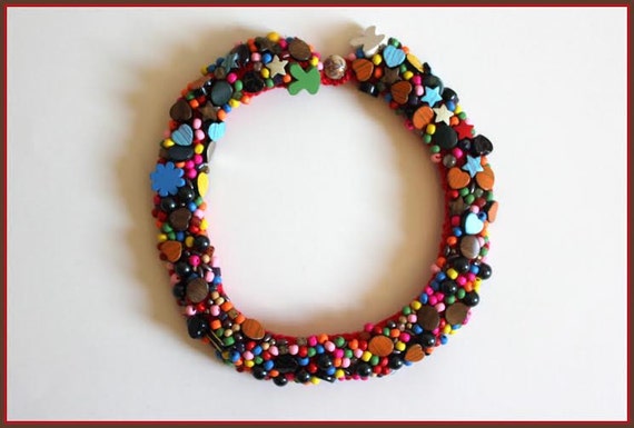 A rainbow necklace. Composition showing all the colours. Multiple beads on 2 strips of red crochet. Joyful and optimistic.