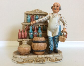 The Old Grocery Store with The Grocer Stocking the Shelves with Bottles Figurine.